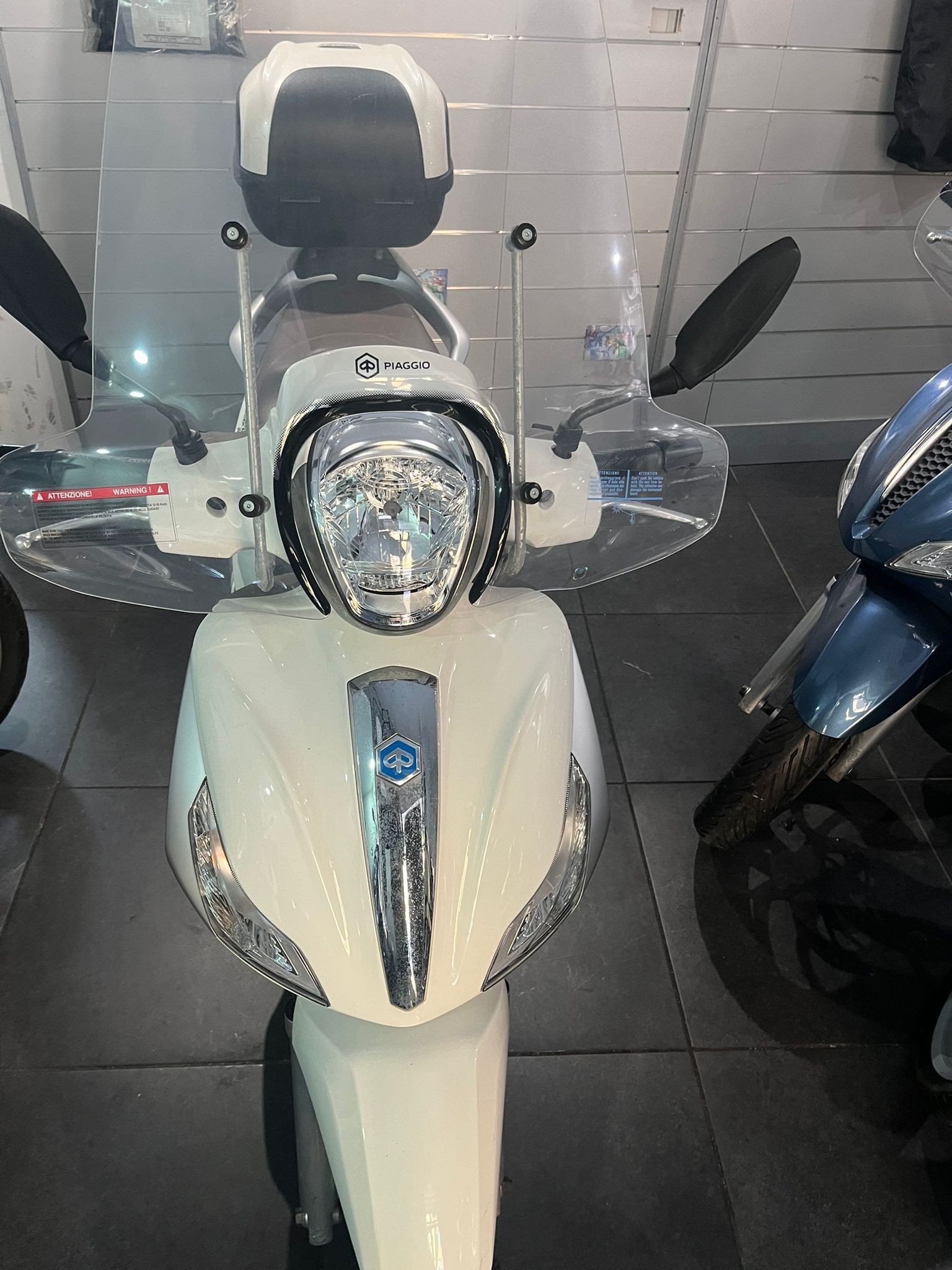 Scooter bianco con parabrezza e bauletto nero, parcheggiato al chiuso.