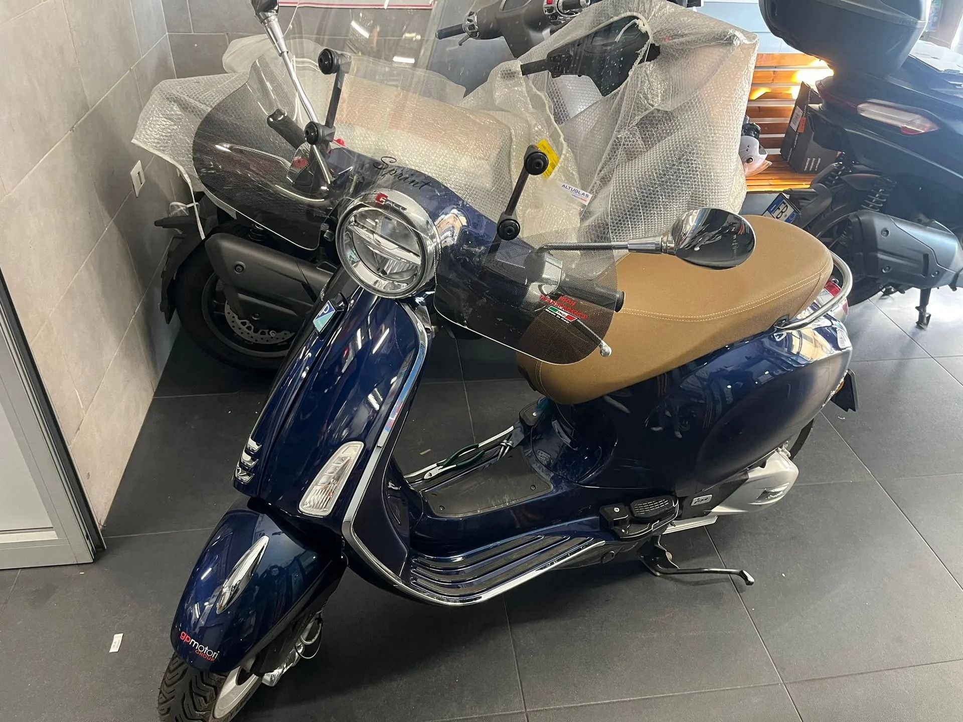 Scooter Vespa blu con sedile marrone parcheggiato in uno showroom.