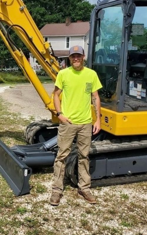 Zanesville Concrete Pros partner Tyler Bond, also owner/operator of Bond Contracting Inc., standing in front of an excavator. Offers concrete driveways, slabs, patios, and coatings in Zanesville, OH.