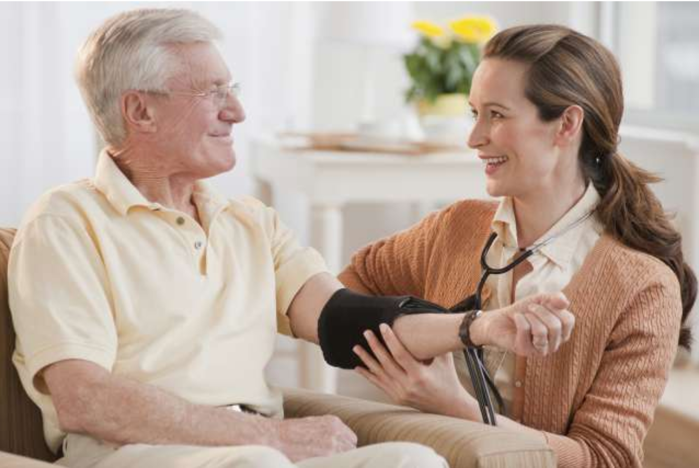 Woman taking an older man's blood pressure in a bright living room