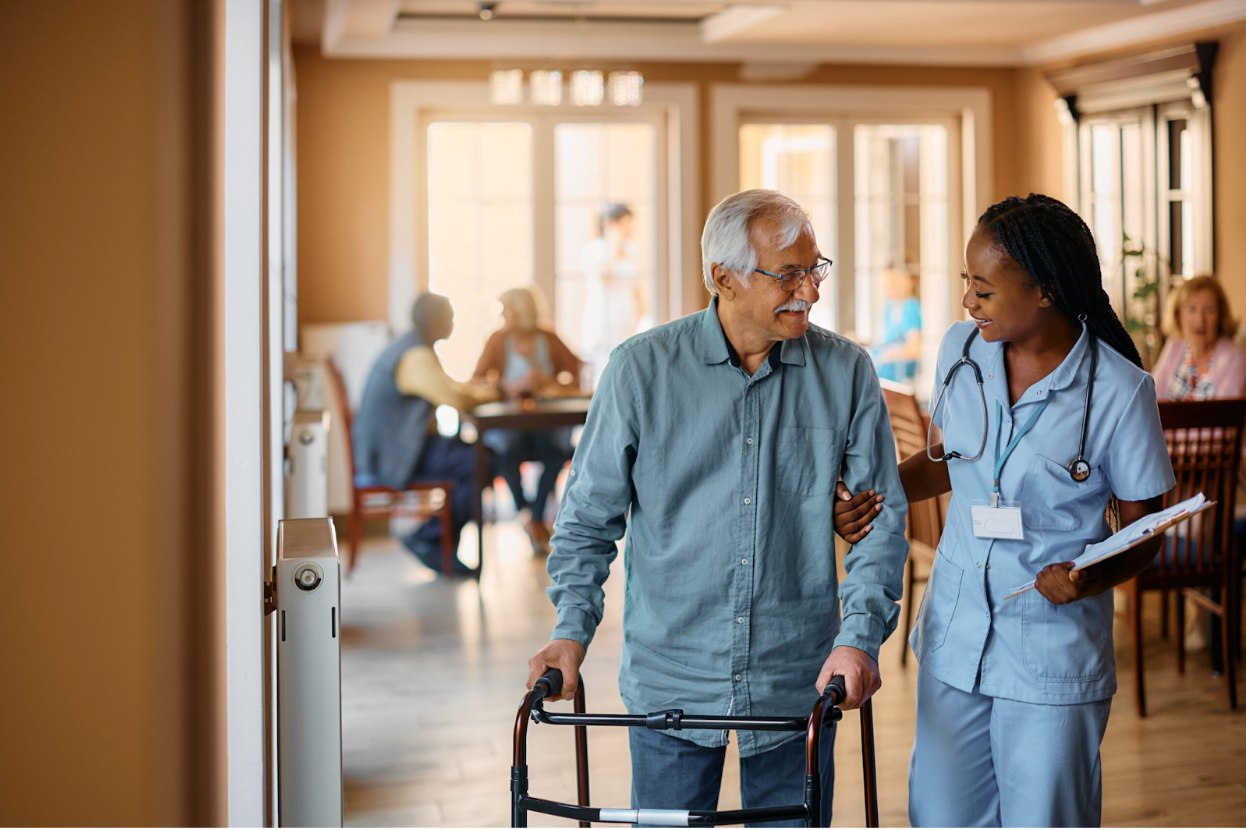 A healthcare worker assists an elderly person using a walker in a care facility.