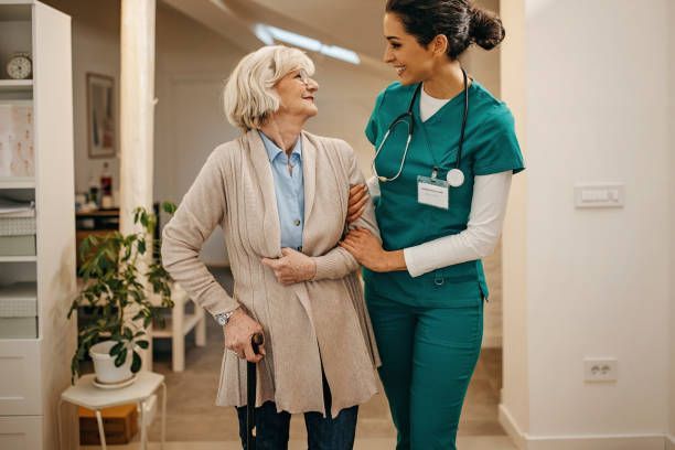 Nurse assisting elderly woman walking with a cane in a brightly lit hallway.