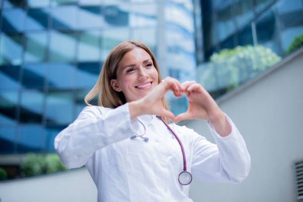 Cardiologist making heart shape with hands in front of hospital.