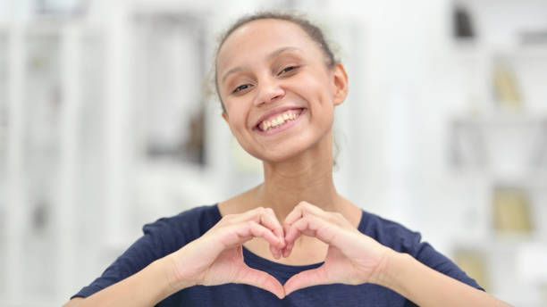 Woman forming a heart shape with her hands, smiling, indoors.