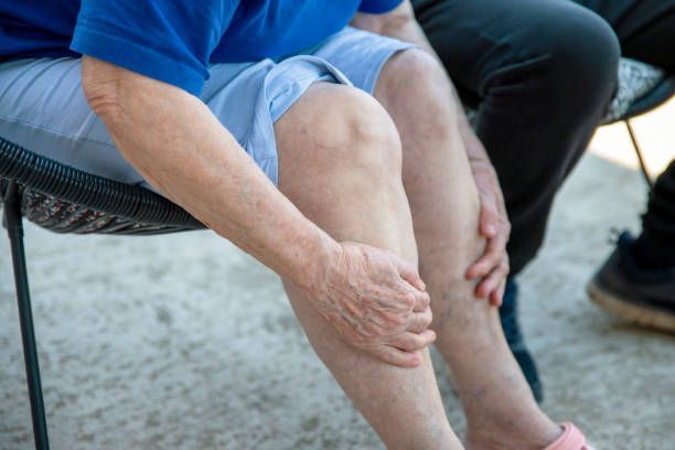 Person sitting, holding legs. Knees visible, light skin. Wearing blue shirt, gray shorts, and pink shoes.