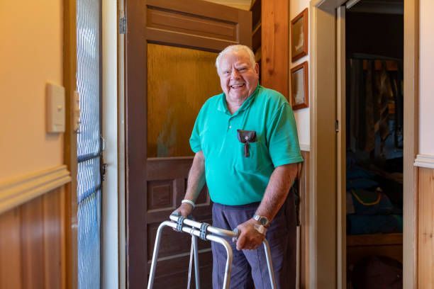 Elderly person using a walker in a doorway, wearing a teal shirt.