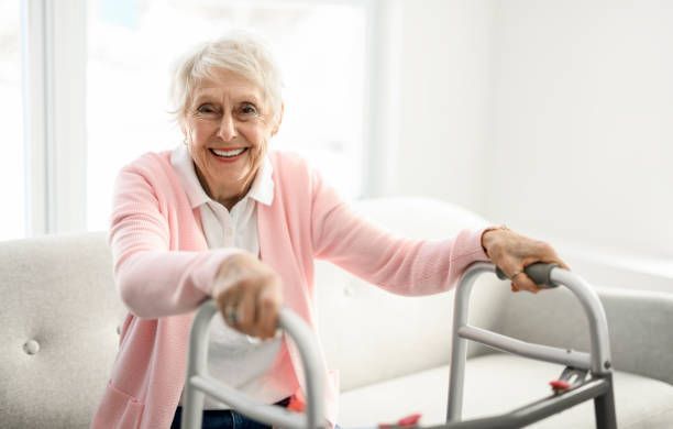 Woman smiles while using a walker in a well-lit living room, holding the handles.