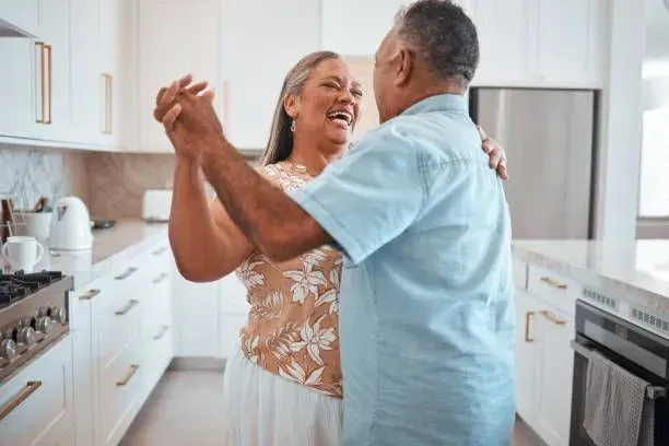 An elderly couple is dancing together in a kitchen.