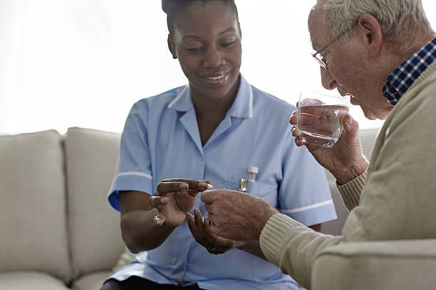 A nurse gives medication to an elderly man. She is smiling as he takes a pill with water.
