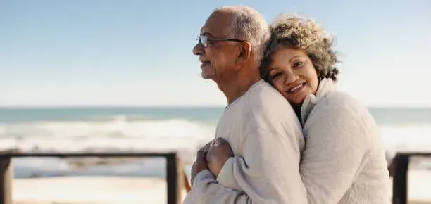 An elderly couple is hugging each other on the beach.