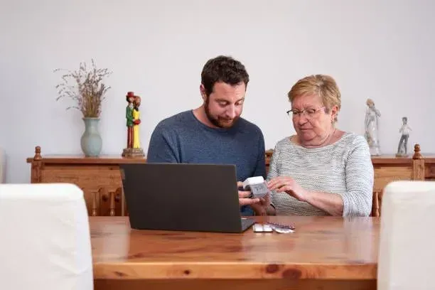 A man and a woman are sitting at a table looking at a laptop.