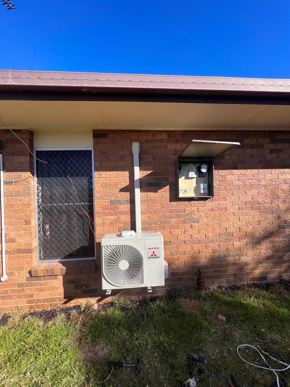 An Outdoor Compressor Hanging on the Brick Wall — Electrician in Armidale, NSW