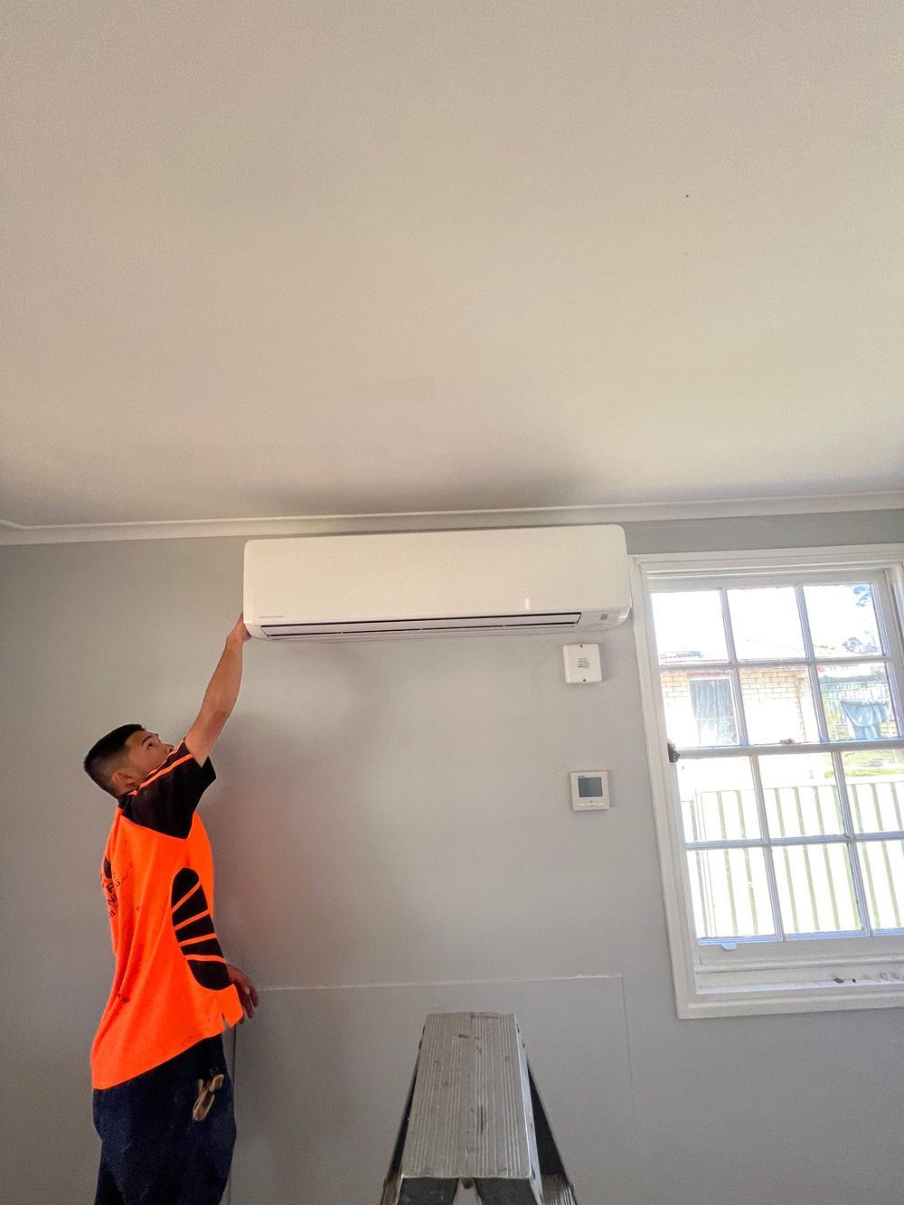 An Electrician Checking the Air-Conditioner in a Bedroom — Electrician in Laurieton, NSW