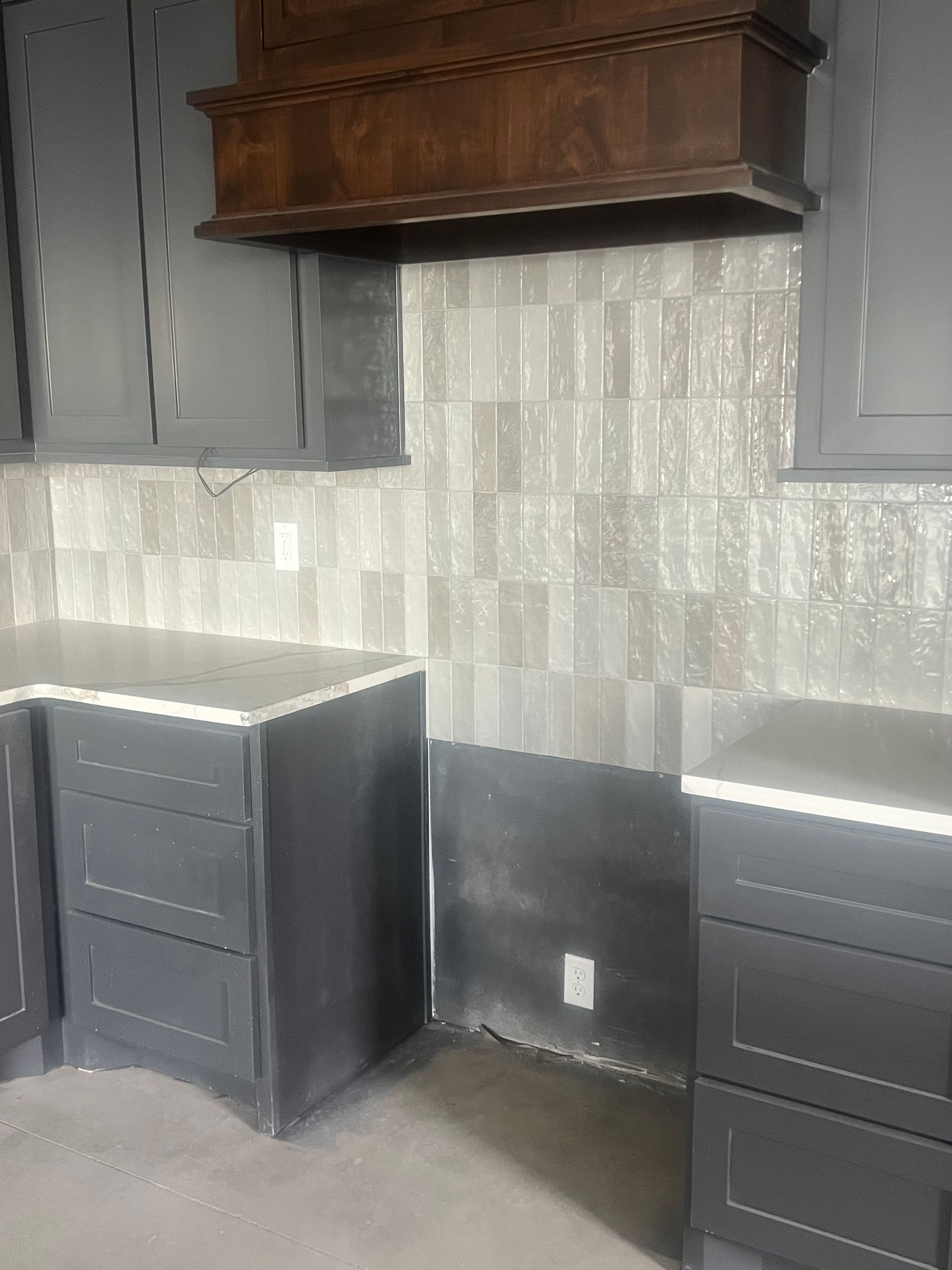 Kitchen with dark gray cabinets, light gray backsplash, and wood hood over stove area.