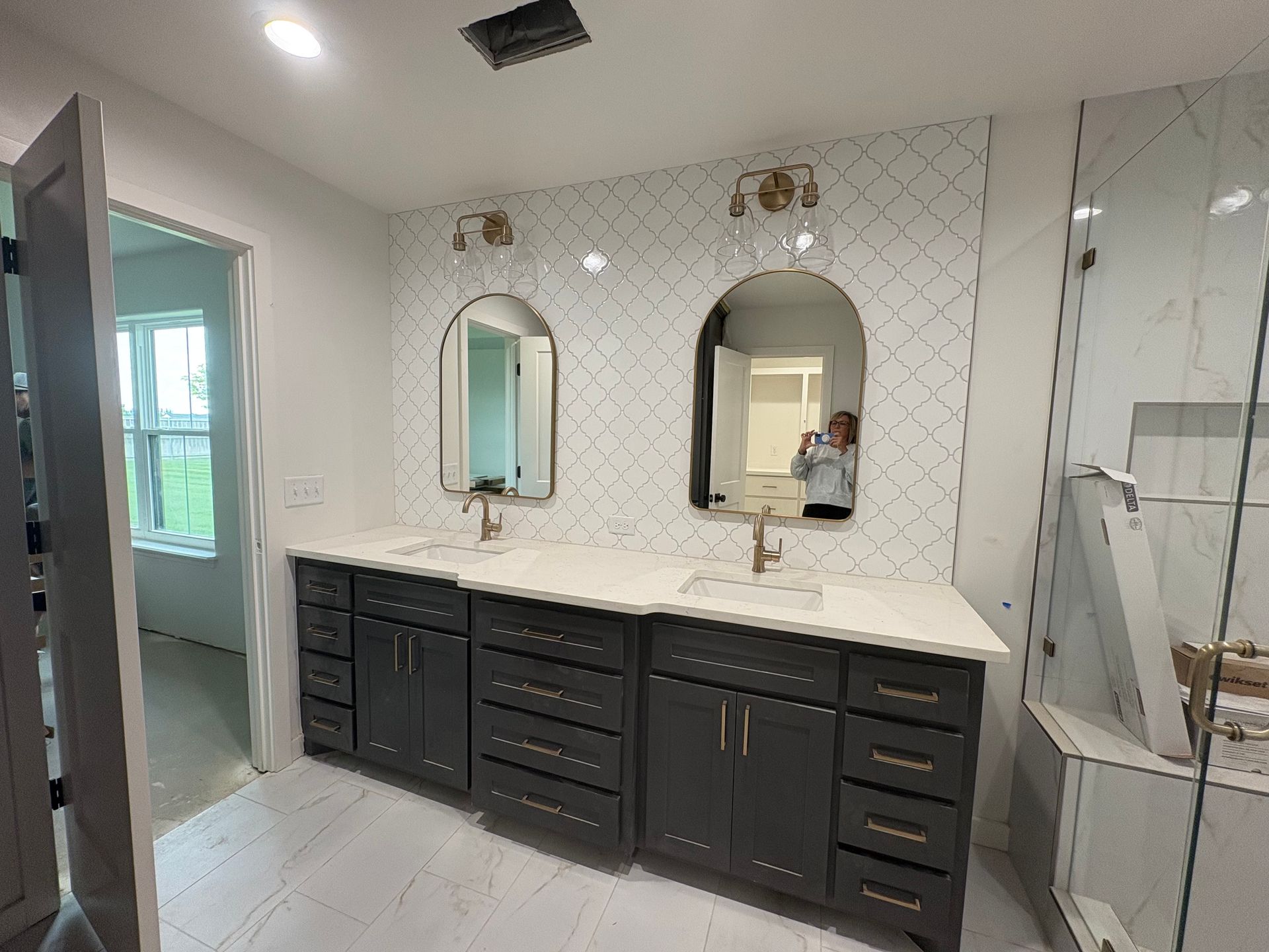 Bathroom with dark gray double vanity, arched mirrors, and white tile backsplash.