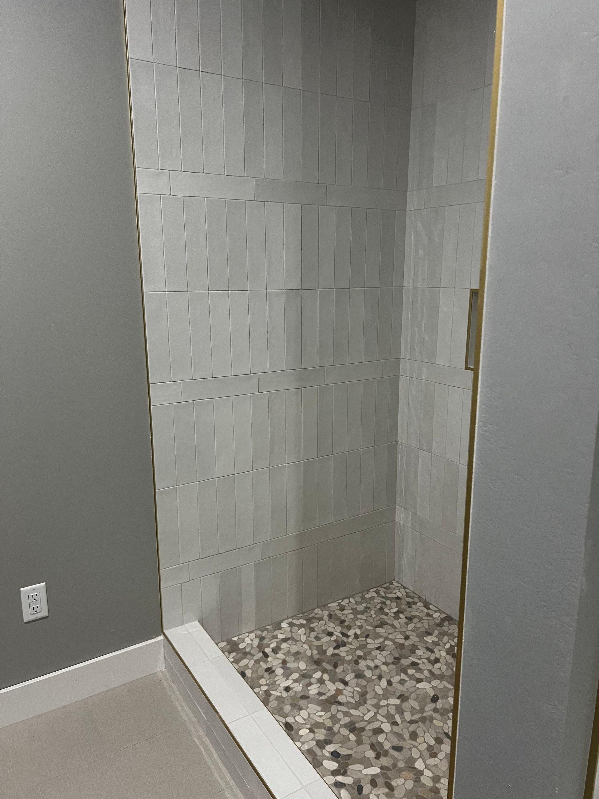 Shower stall with gray walls, pebble floor, and vertical patterned tile.
