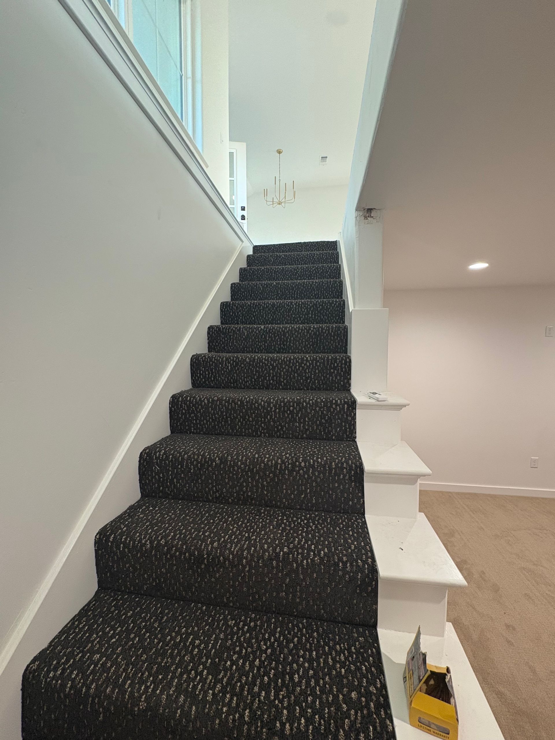 Staircase with black speckled carpet leading to upper level with white walls and trim.