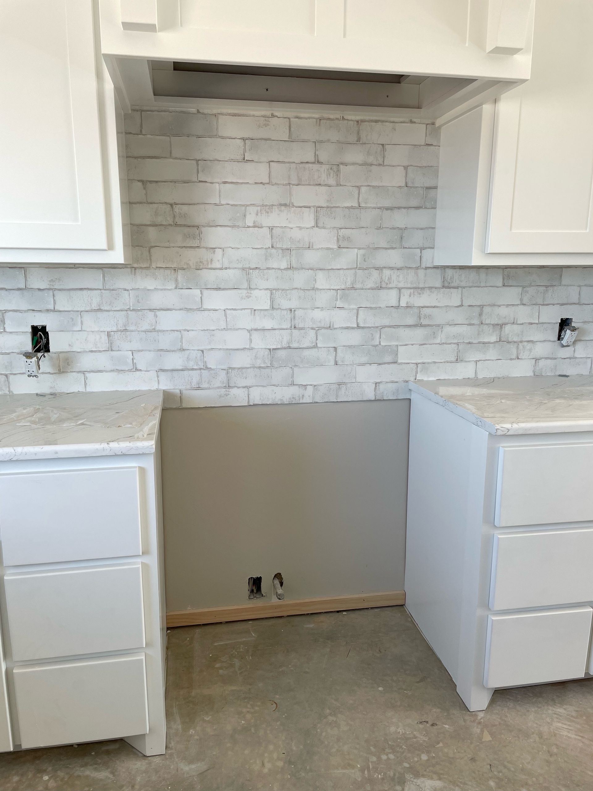 Kitchen under construction; white cabinets, brick backsplash, gray wall.