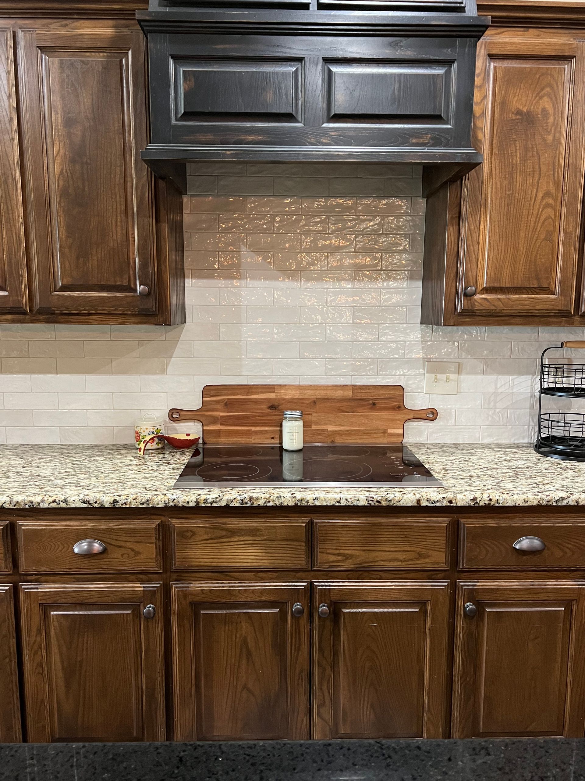 Kitchen with dark wood cabinets, black range hood, light backsplash, and granite countertop. Kitchen with dark wood cabinets, black range hood, light backsplash, and granite countertop.