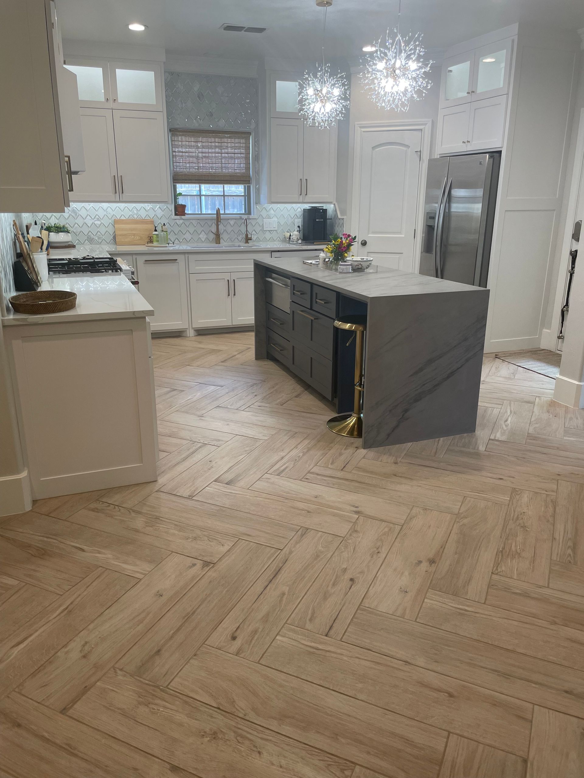 Kitchen with white cabinets, gray island, and herringbone wood-look tile flooring.