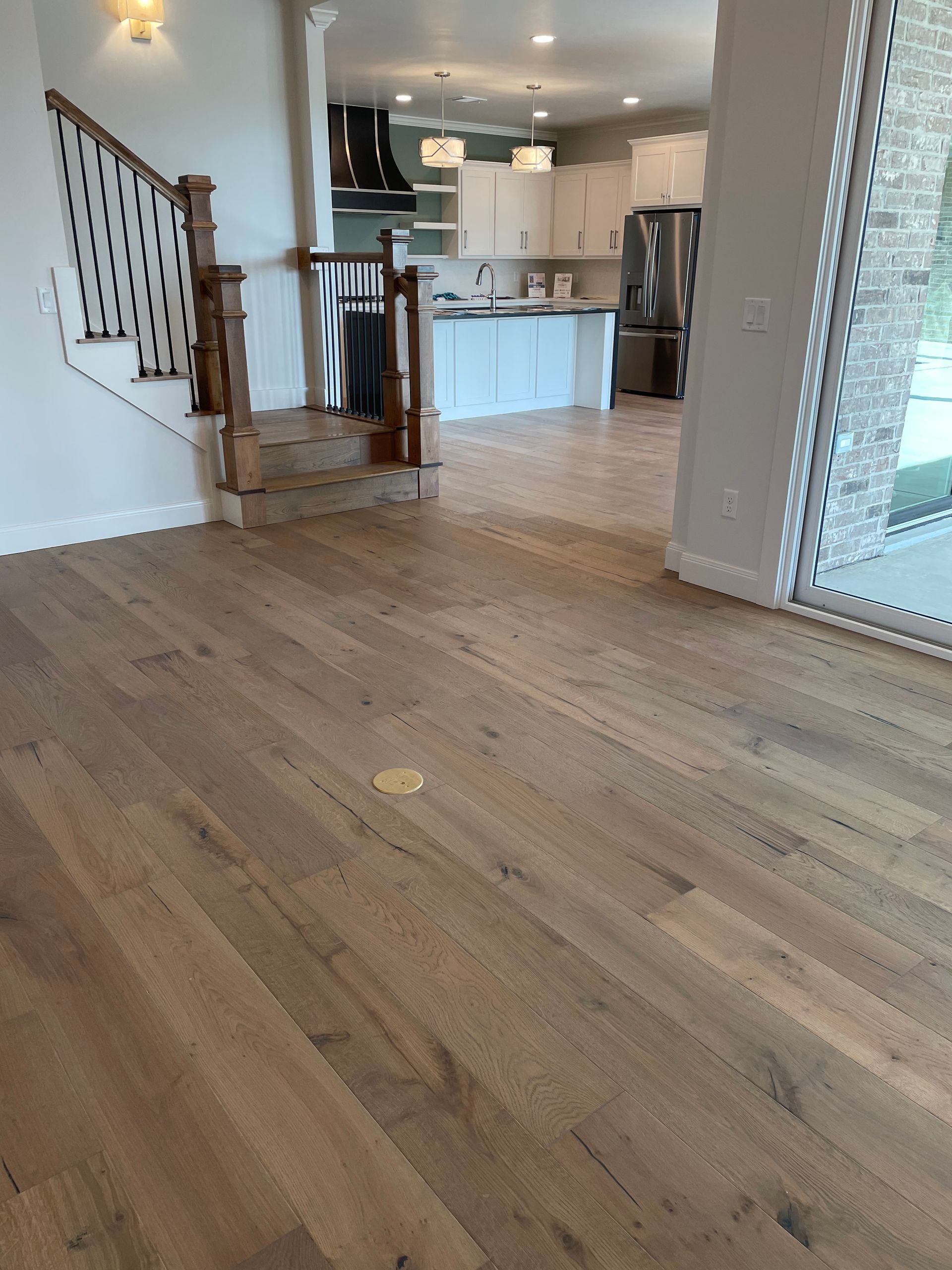 Light wood flooring in a home, with stairs on the left leading to kitchen with white cabinets.