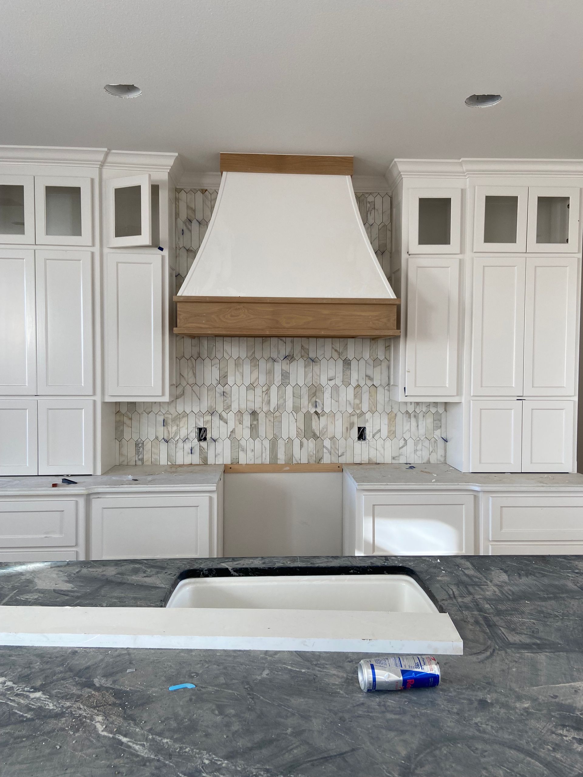 Kitchen cabinets with a white range hood and backsplash during renovation.