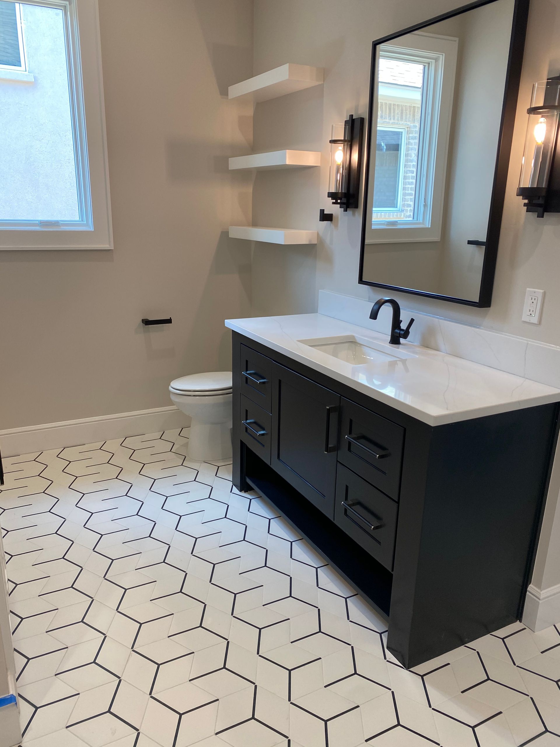 Bathroom with hexagonal black and white floor tiles, dark vanity, white countertop, and floating shelves.