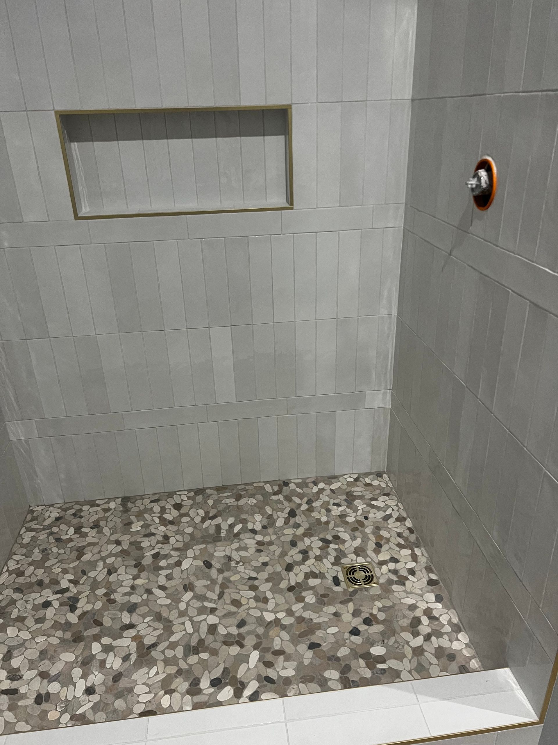 Shower with gray tiled walls and a mosaic tile floor, built-in shelf, and showerhead.