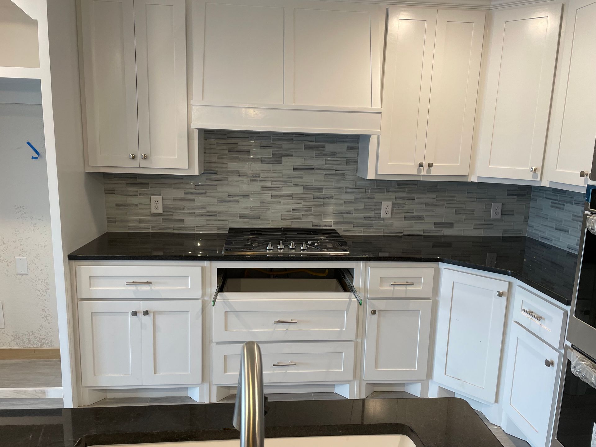 White kitchen with black countertops, gas range, gray backsplash, white cabinets.