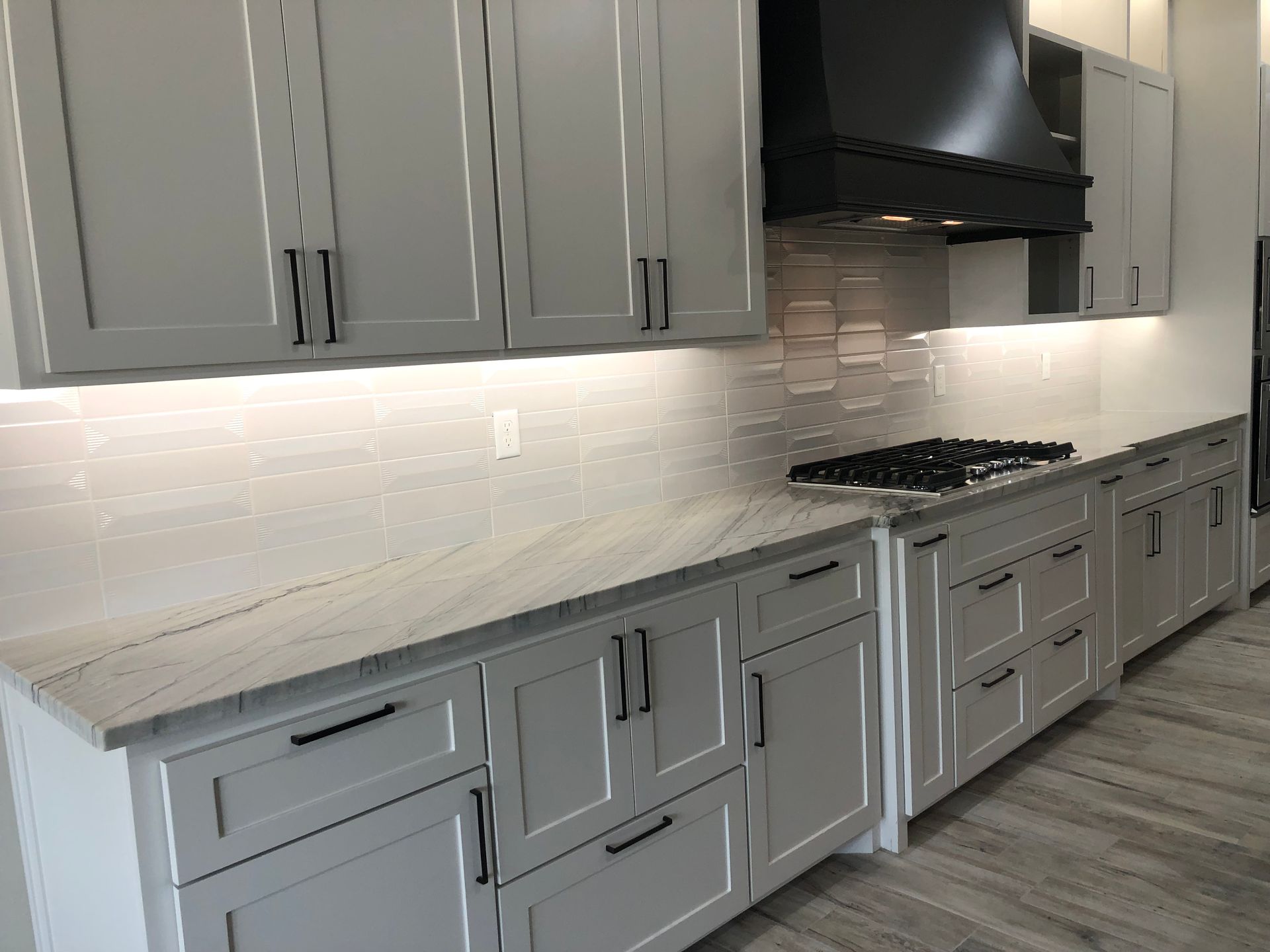 Kitchen with gray cabinets, white countertops, and a black range hood.
