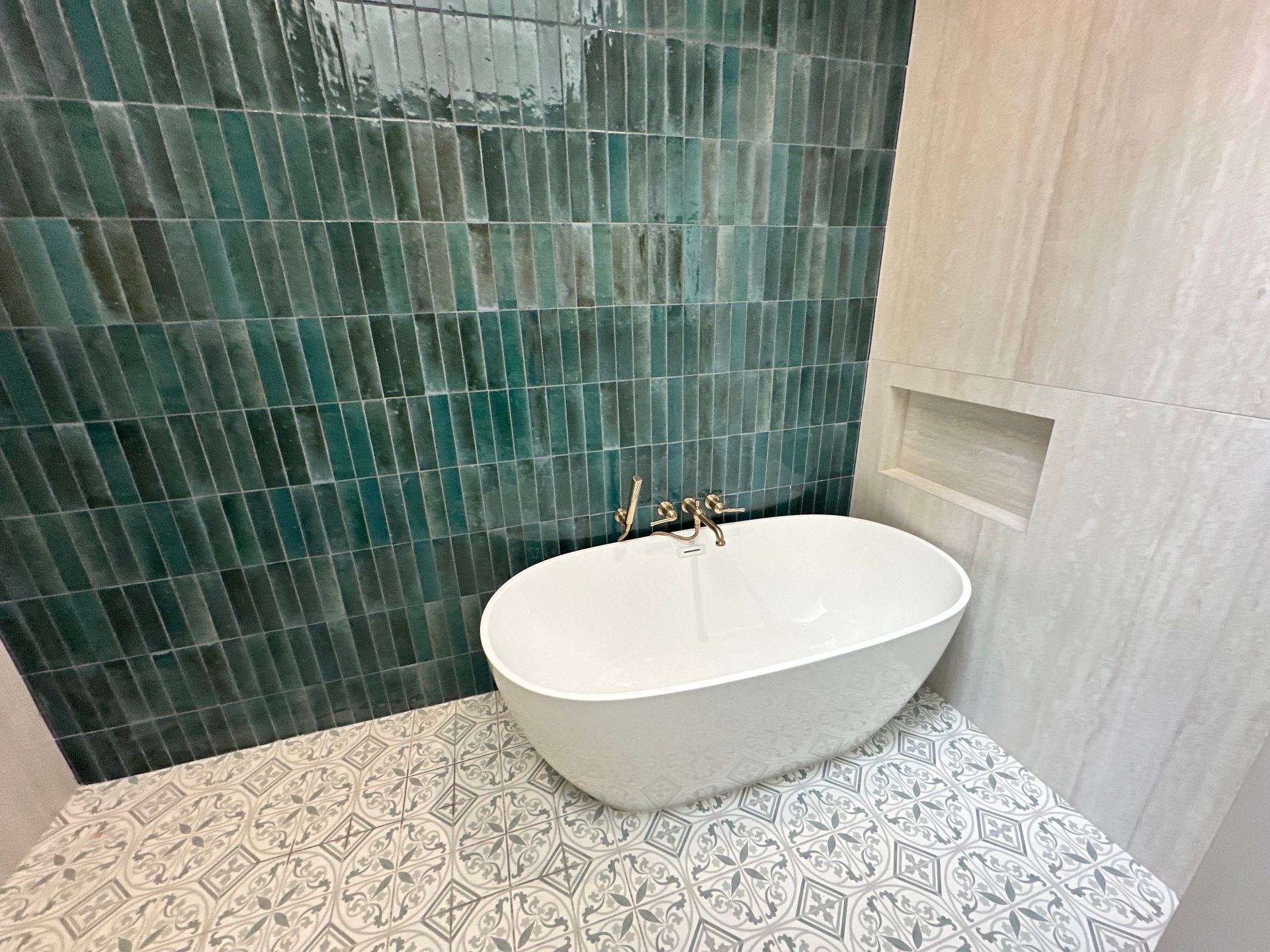 Bathroom with emerald green tile wall, white tub, and patterned floor.