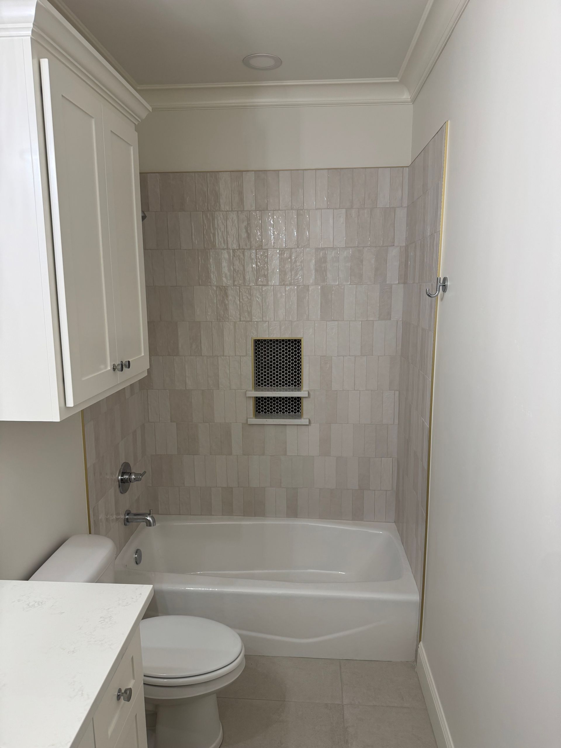 Bathroom with white cabinets, tub, and toilet. Tile wall in neutral tones.