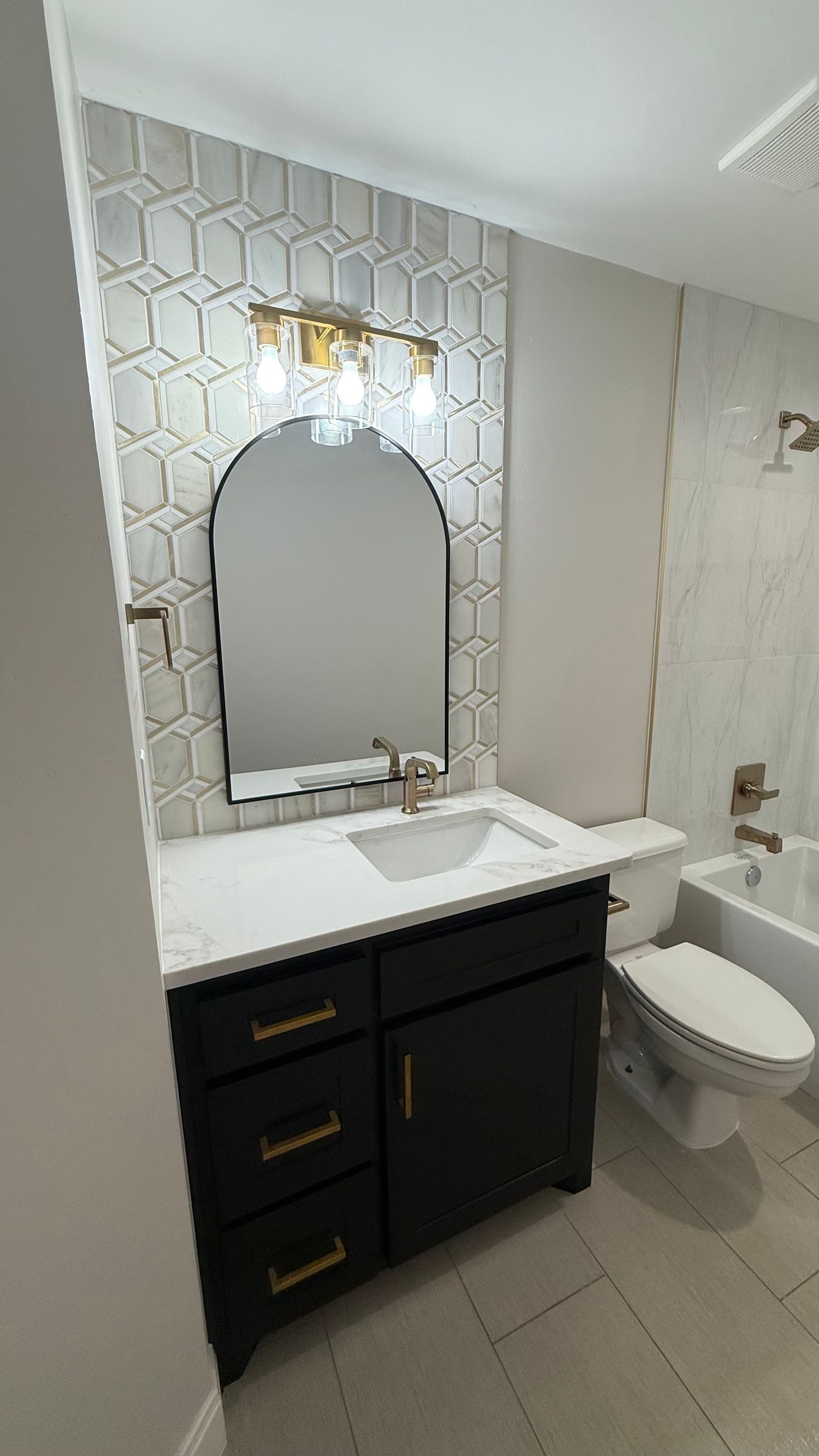 Bathroom with black vanity, white countertop, hexagon tile backsplash, and arched mirror.