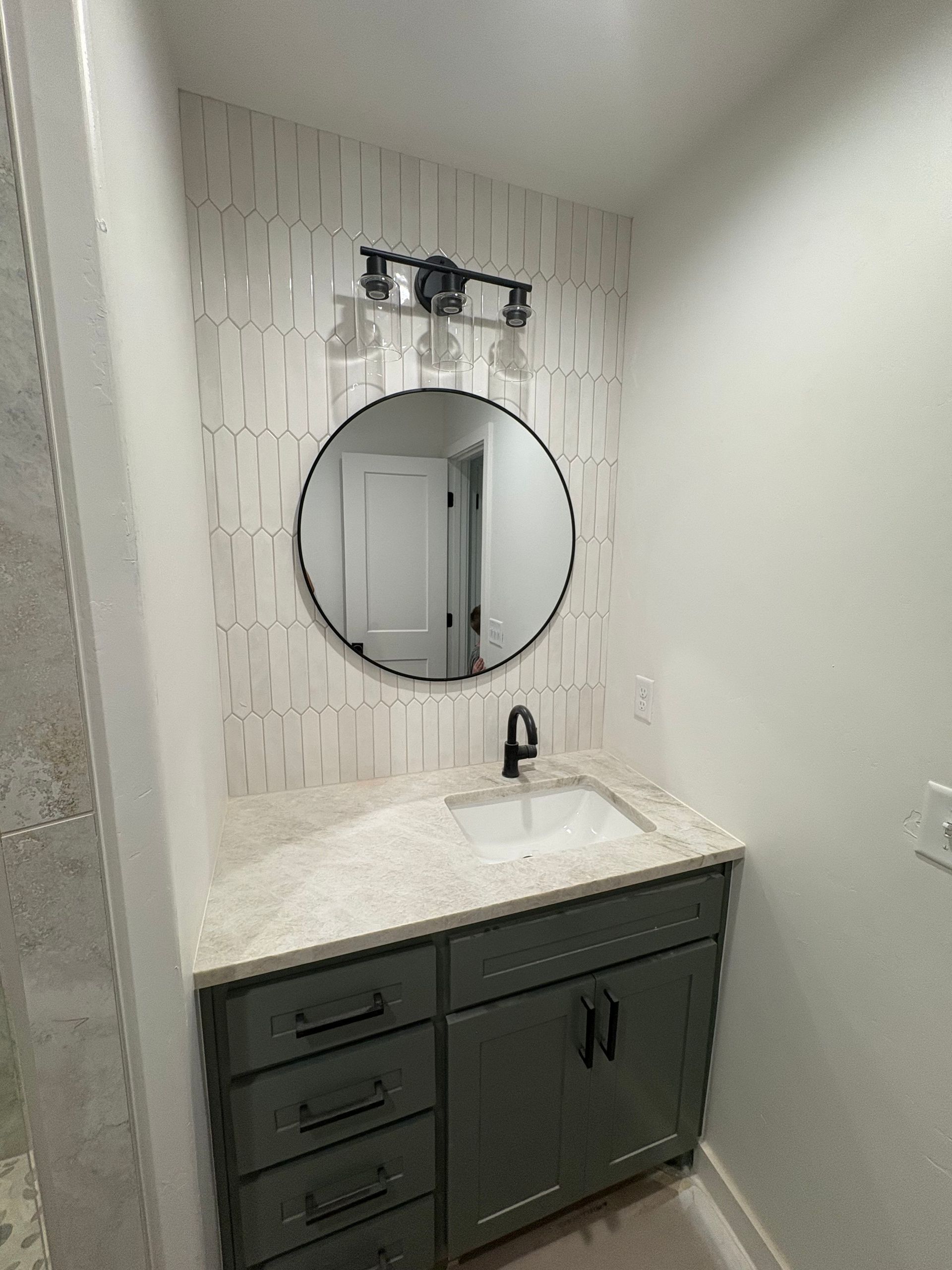 Bathroom with a green vanity, round mirror, and patterned tile backsplash.
