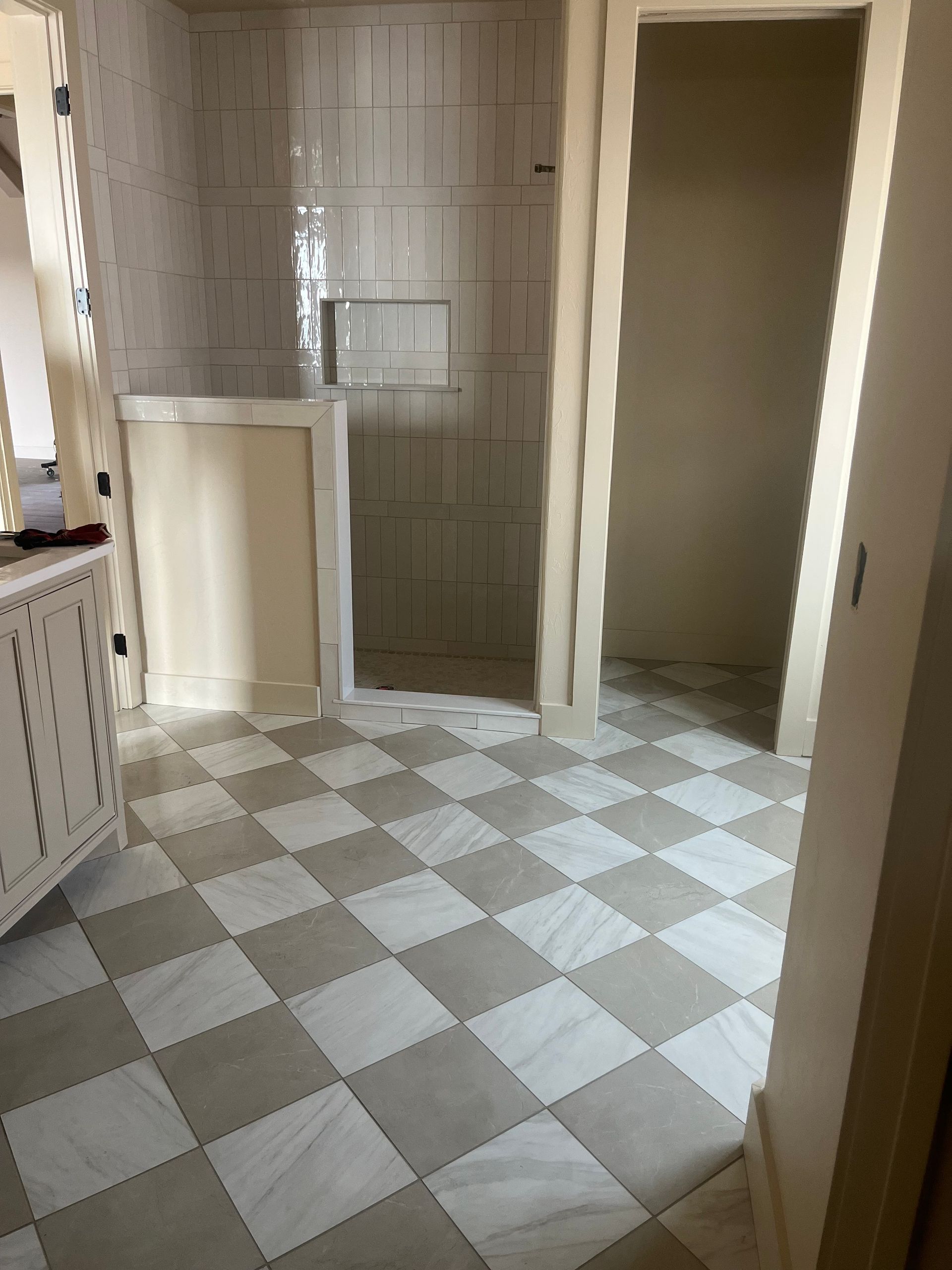 Bathroom with checkered floor, neutral walls, and shower area. Open doorway on right.