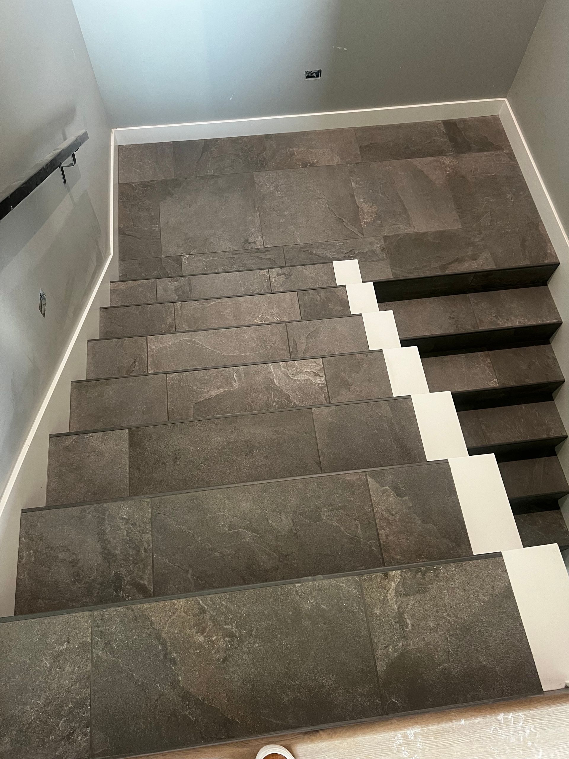 Stone-tiled staircase with white risers and a black handrail.