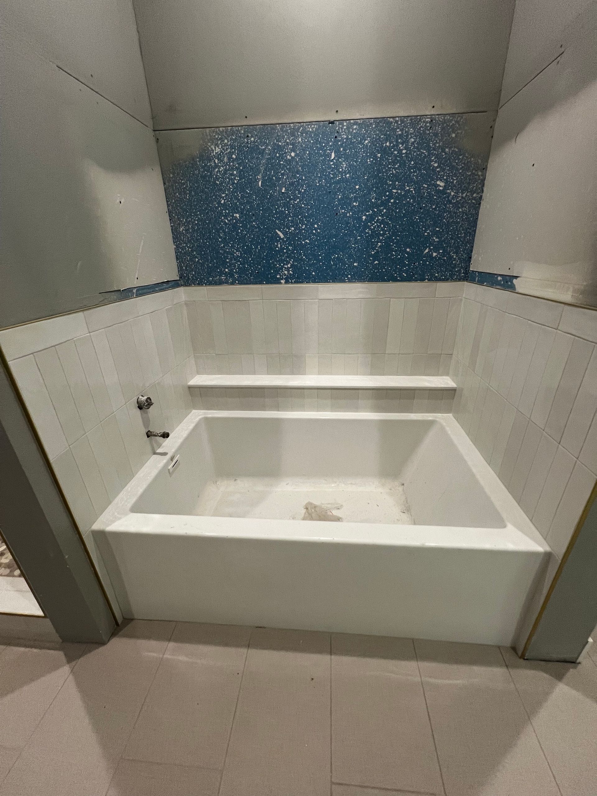 White bathtub with blue mosaic tile accent; construction site setting.