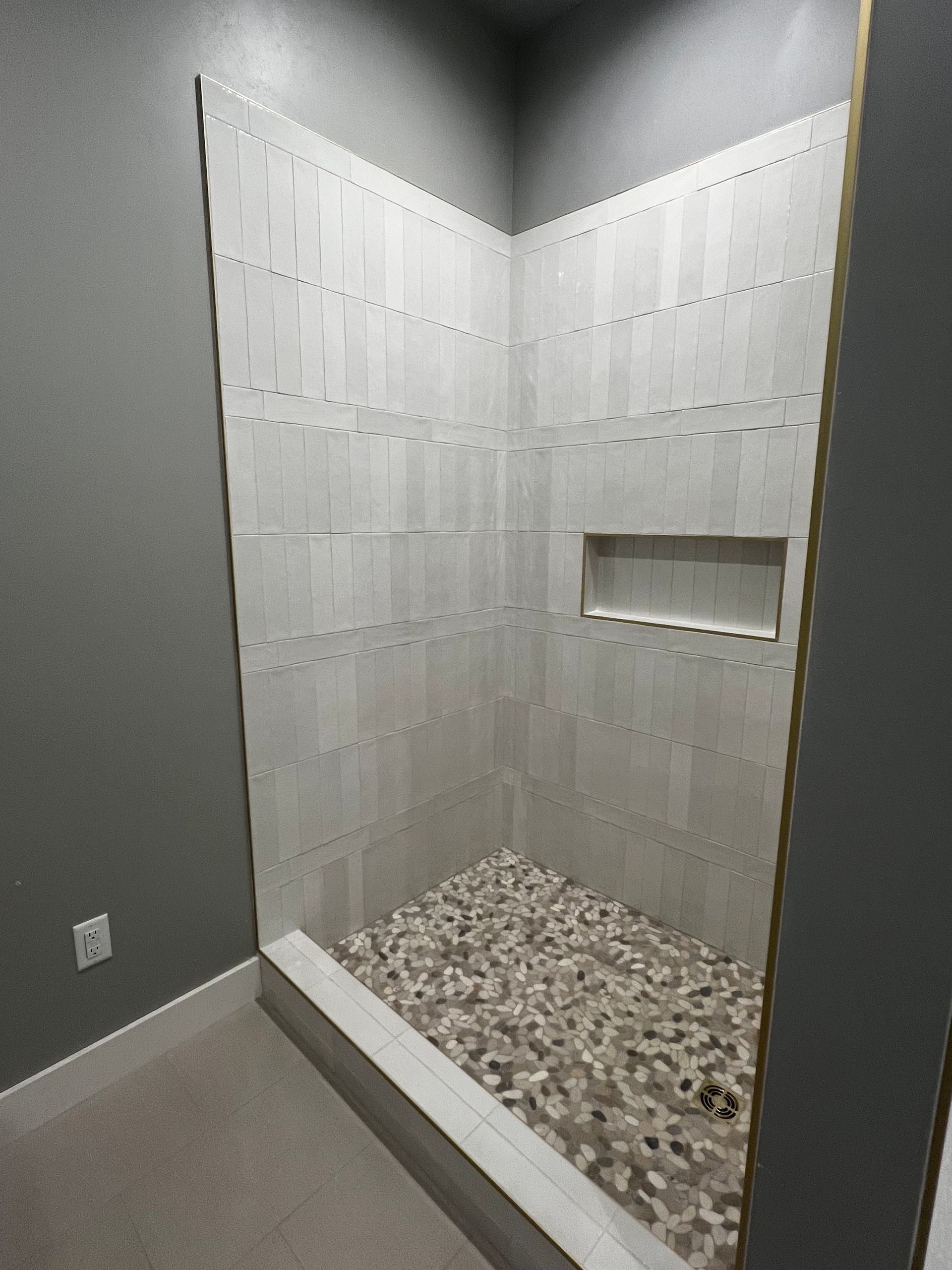 Shower stall with pebble floor and tiled walls; includes built-in shelf.