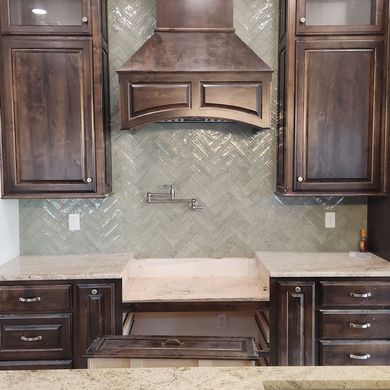 Dark wood kitchen cabinets, range hood, and light green herringbone tile backsplash.