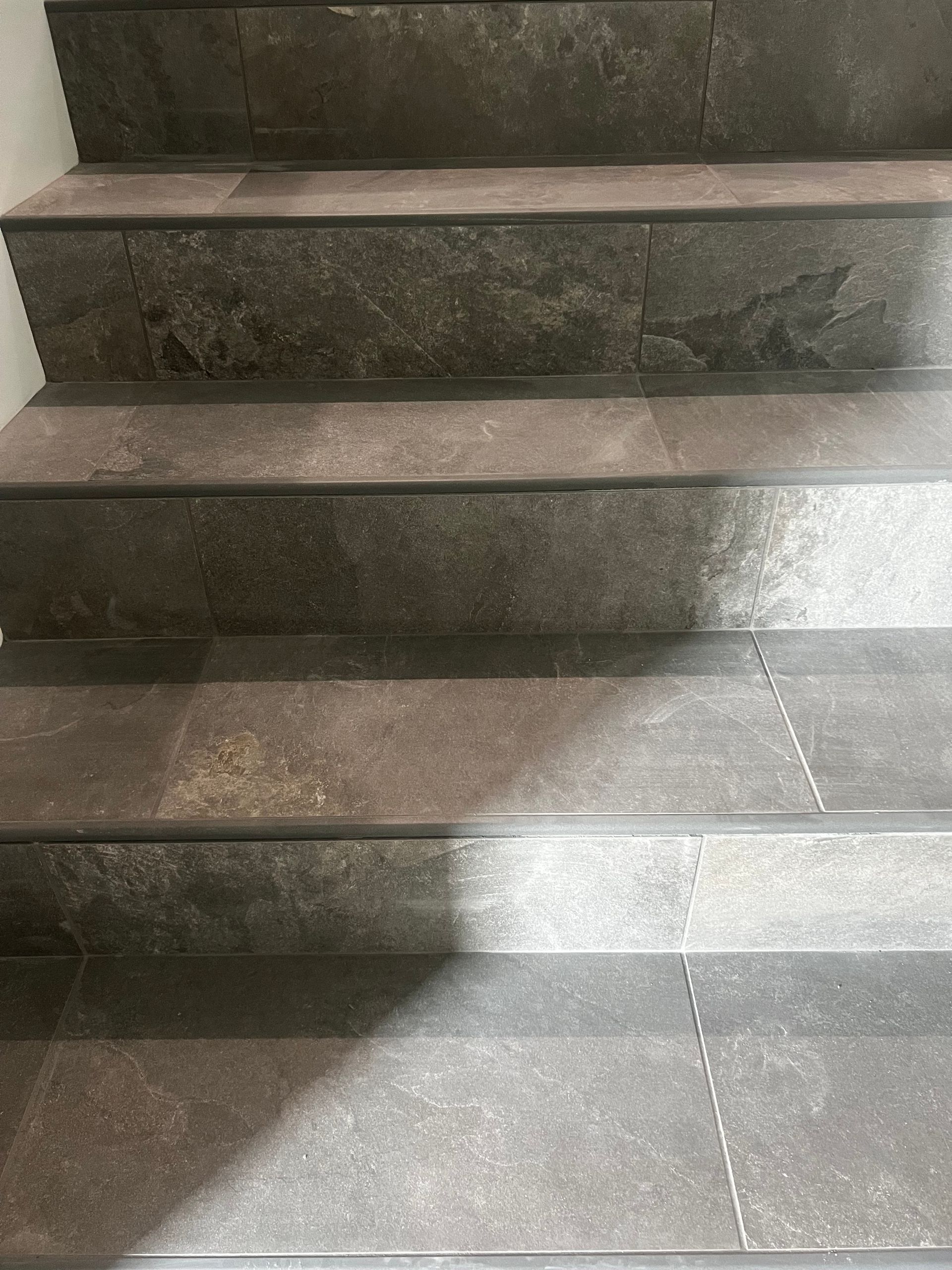 Staircase with dark gray tile steps; shadow across lower steps.