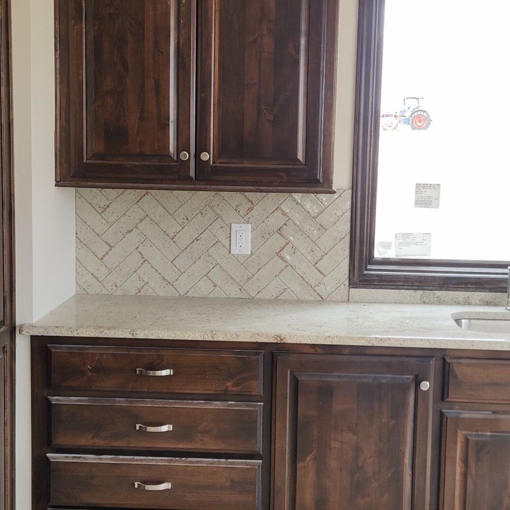 Dark wood cabinets with light countertop and herringbone backsplash tile.