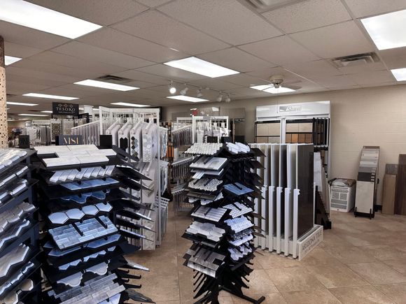 Tile showroom with displays of various tile samples; neutral tones, overhead lighting.