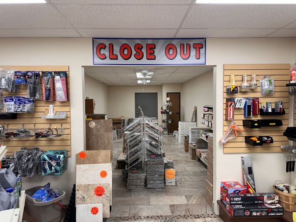 A store interior with a CLOSE OUT sign over an aisle lined with shelves of merchandise.