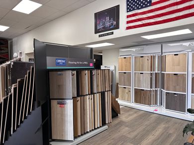 Flooring showroom with carpet and wood samples displayed. American flag hangs on the wall.