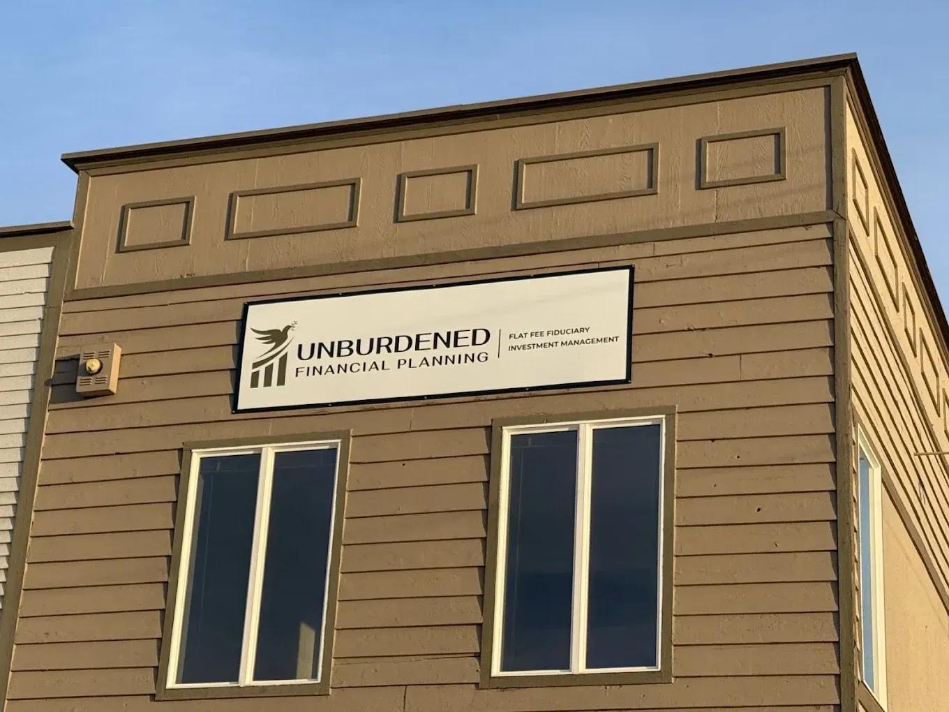 The tan exterior of a building featuring a sign for Unburdened Financial Planning above two windows.