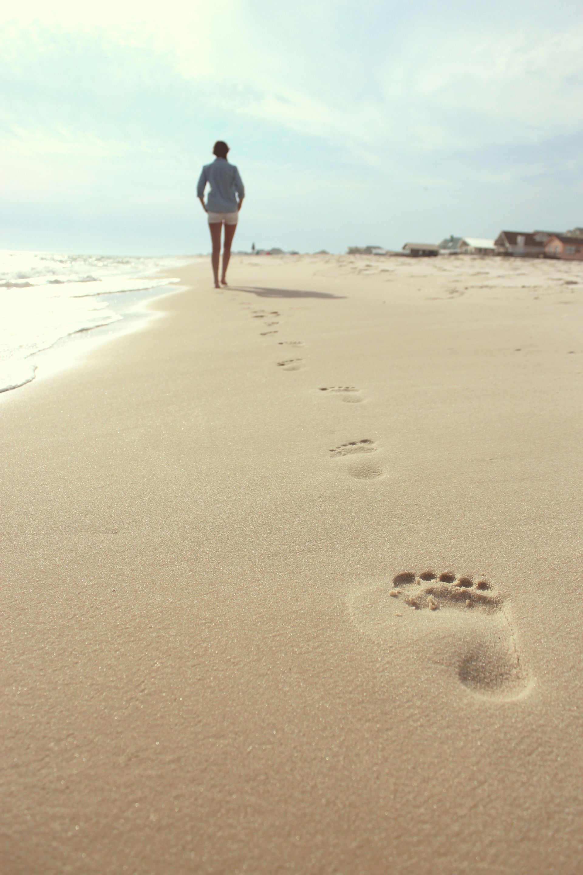 A person walks along a sandy beach, leaving a trail of footprints leading toward the shore.