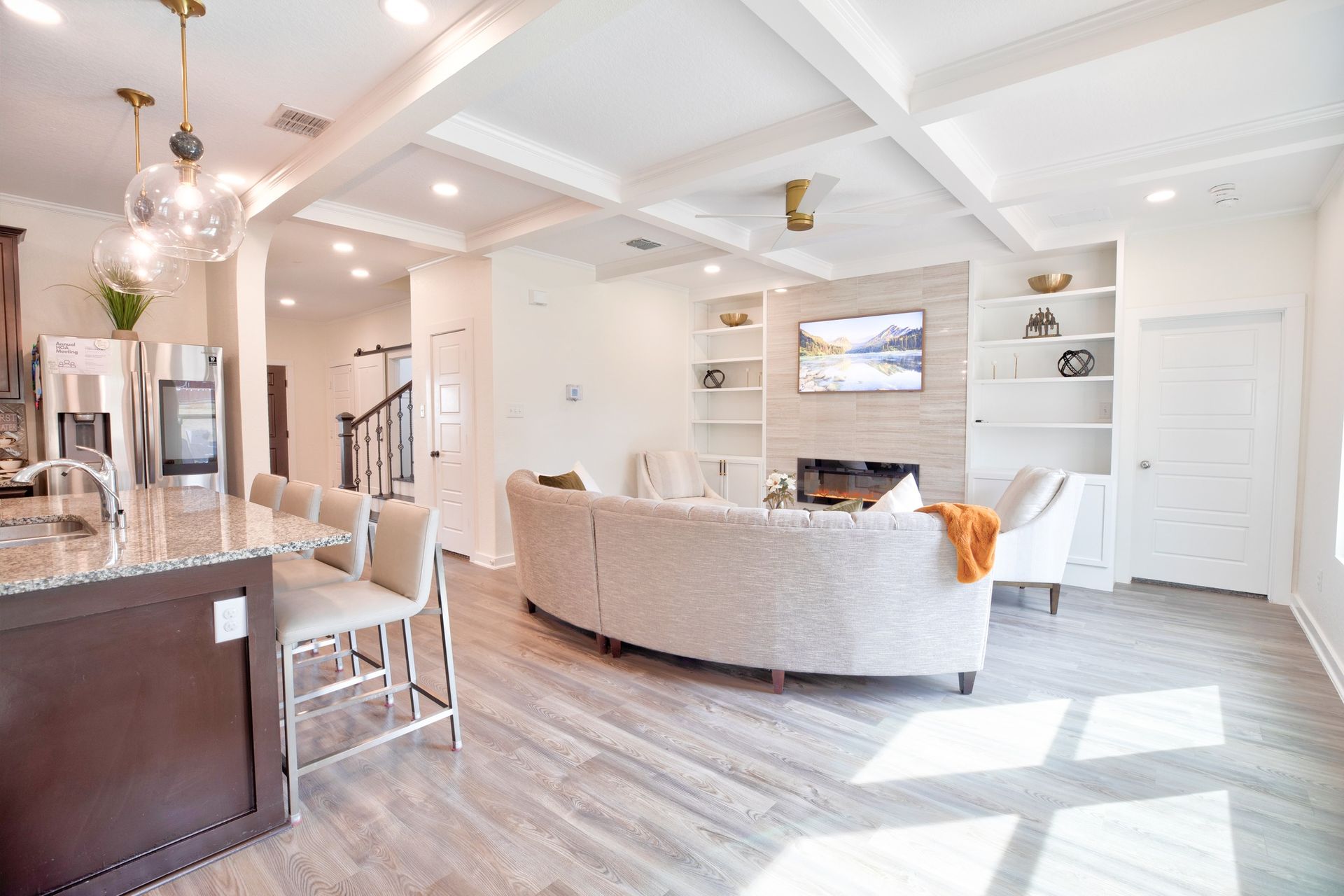 Modern living room with white walls, hardwood floors, curved sofa, fireplace, and kitchen island with bar stools.