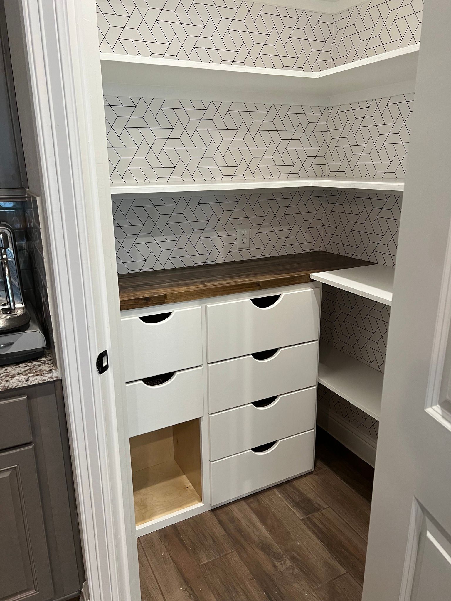 A white pantry with drawers and shelves; the back wall has a black dotted pattern.