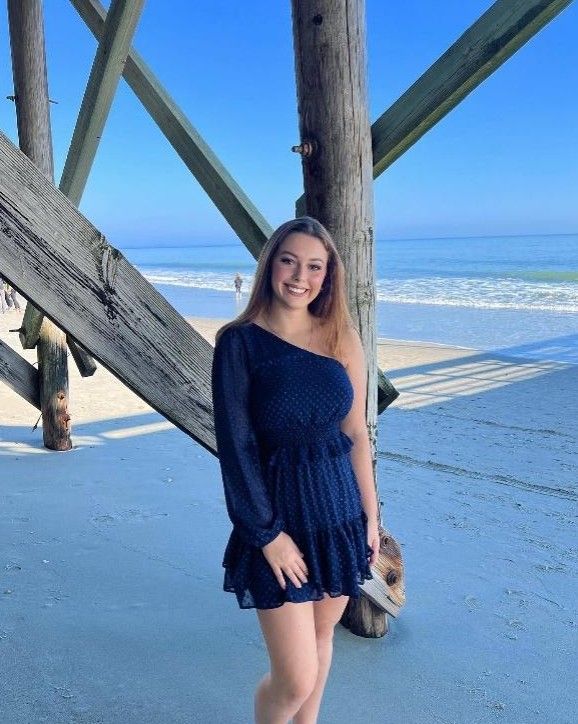 Family posing outdoors: father with a child on his shoulders, pregnant mother, and another child; near a stream.
