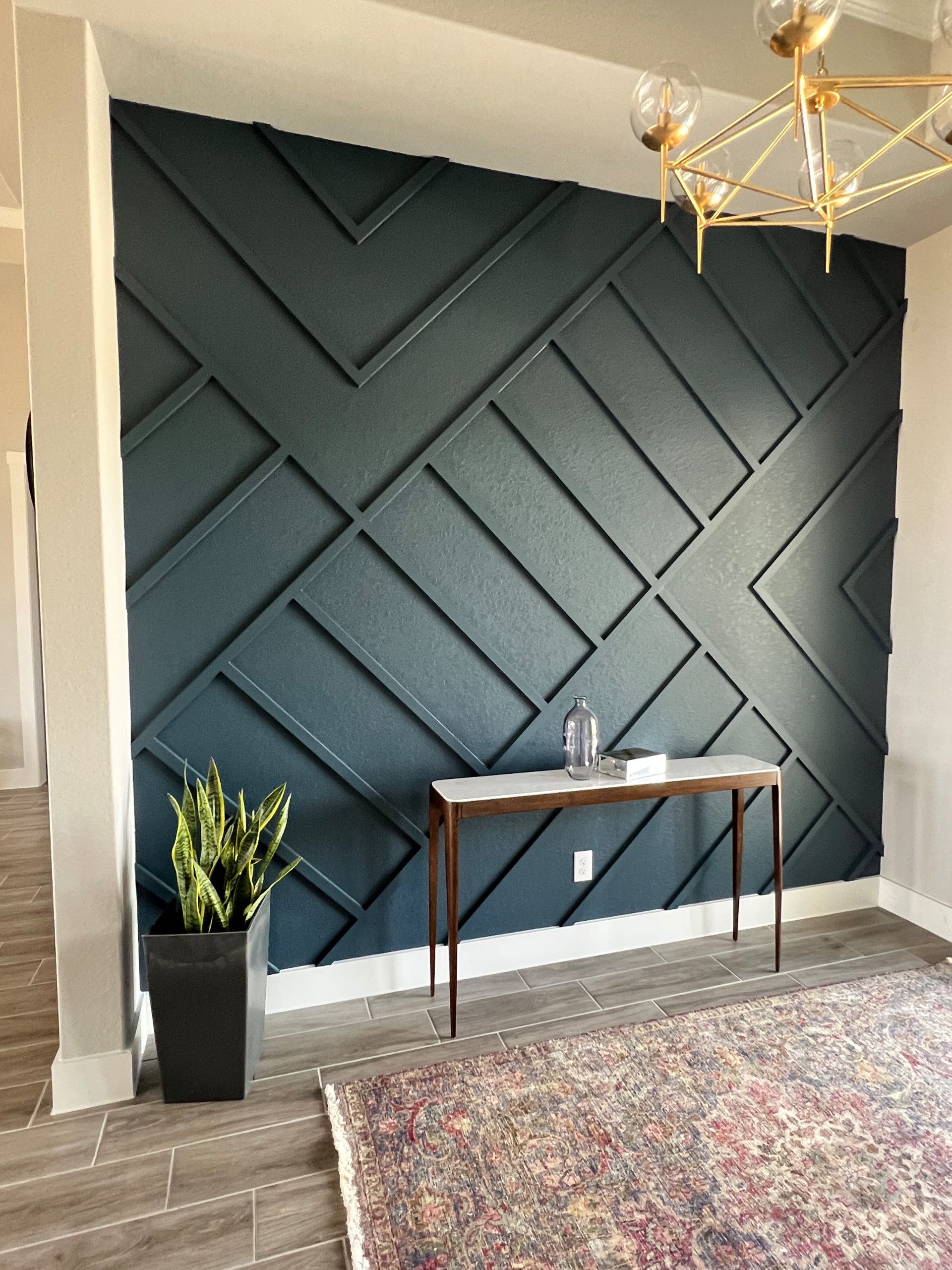 Teal accent wall with geometric trim design, console table, and rug in a living space.